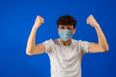 COVID-19 'la dövüş. Coronavirus portresi. Maske takan yakışıklı genç adam. Stüdyoda mavi arka planda izole edilmiş. Avrupalı erkekler. COVID-19 kavramı.
