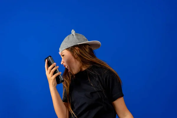 Arg liten flicka med vacker brunett hår över blå bakgrund skriker på telefonen, har ett argument. — Stockfoto