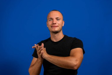 Gülümseyen Yakışıklı Adam Mavi stüdyo arka planında el çırpıyor