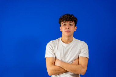 Mavi stüdyo arka planında kollarını kavuşturmuş gülümseyen yakışıklı adam.