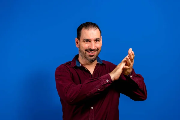 Homem barbudo hispânico atraente batendo palmas excitadamente depois de testemunhar algo apoteose, sorri satisfeito com o espetáculo. Isolado em fundo estúdio azul — Fotografia de Stock