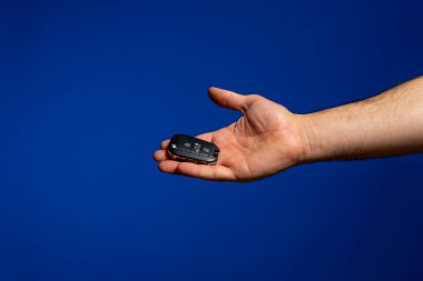 Mans hand generously offering his car keys, isolated on blue studio background