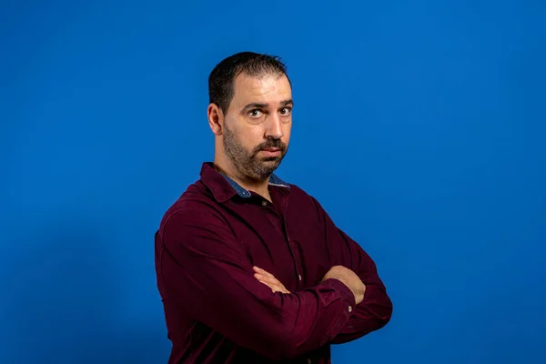 Retrato de homem barbudo espanhol sério e preocupado com braços cruzados, isolado em fundo estúdio azul — Fotografia de Stock