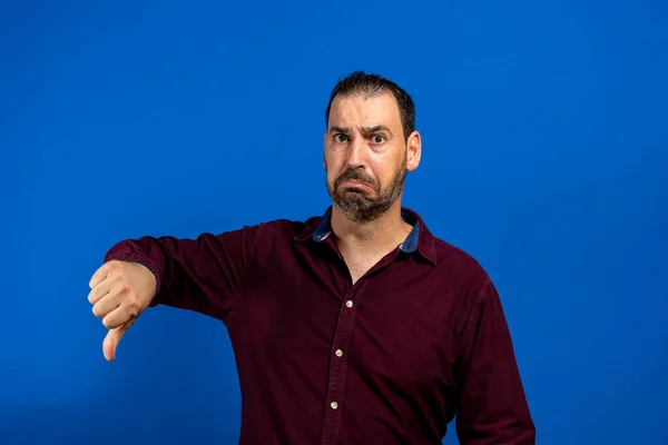 Mladý ležérní muž dělat palce dolů negativní znak ruky na modrém pozadí. — Stock fotografie