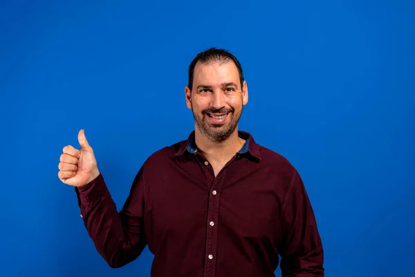 Retrato de homem alegre em roupas básicas sorrindo e mostrando os polegares para cima da câmera isolada sobre fundo azul — Fotografia de Stock