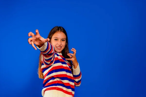 Foto de graciosas manos con garras de niña funky vestidas con un suéter a rayas aislado sobre fondo azul Fotos de stock