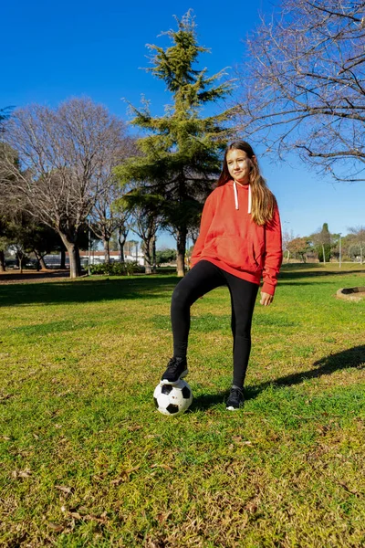 Mooi meisje stapt op een voetbal in een uitdagende positie, ze doet sport in een prachtig park met natuurgras. Gezond leven. — Stockfoto