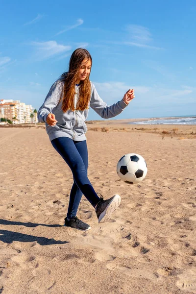 Klein meisje met een voetbal op het strand. Vakantie sport spelletjes, sport, vakantie, levensstijl. — Stockfoto