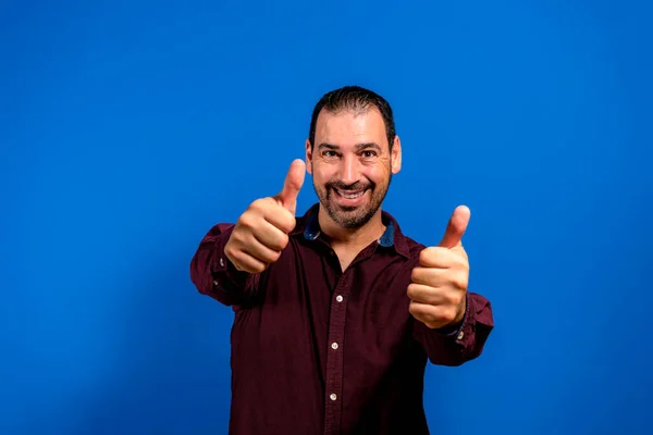 Jonge knappe man in paars shirt die positief gebaar met de hand goedkeurt, glimlacht en blij is voor succes. winnaar gebaar — Stockfoto