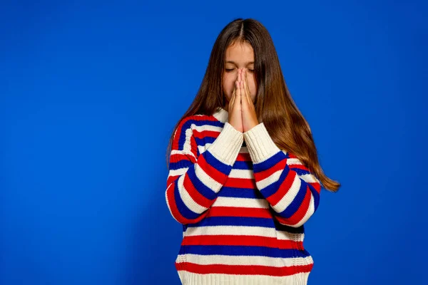 Liten kaukasisk flicka isolerad på blå bakgrund hålla händer i be nära munnen, känner sig säker — Stockfoto