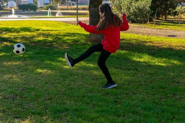Hermosa niña jugando al fútbol en un bonito parque con césped natural en un día soleado de invierno. Ejercicio y concepto de vida saludable — Foto de Stock