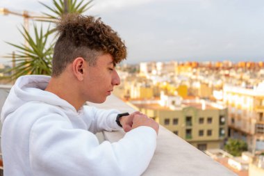 Beyaz kazak giymiş beyaz saçlı genç beyaz bir adam şehrin ufuk çizgisine ciddi ve melankolik bakıyor. Geleceğini ve hayatın ona neler hazırladığını düşünüyorum.