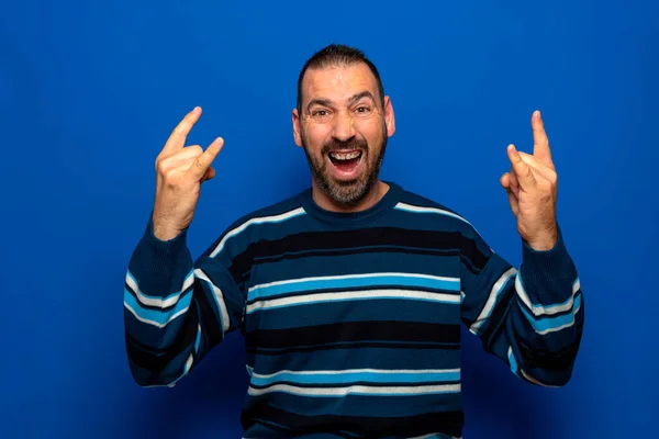 Homem bonito jovem sobre fundo isolado azul gritando com expressão louca fazendo símbolo de rocha com as mãos para cima. Estrela musical. Conceito pesado — Fotografia de Stock