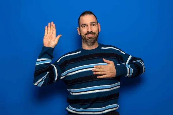 Jovem homem bonito com barba vestindo camisola casual sobre fundo azul Jurando com a mão no peito e palma aberta, fazendo uma promessa de lealdade juramento — Fotografia de Stock