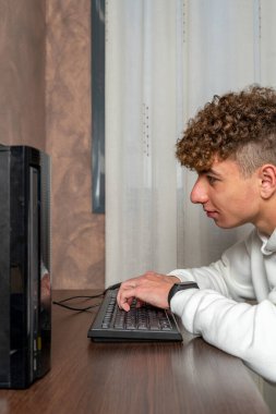 Masaüstü bilgisayarına yoğunlaşmış kıvırcık saçlı genç bir adamın dikey görüntüsü..