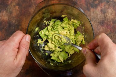 Mans elleri, zengin ve taze bir guacamole hazırlamak için çatalla birkaç avokadoyu kaseye sıkıştırıyor. Sağlıklı gıda konsepti.
