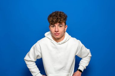 Mavi arka planda izole edilmiş, stüdyo portresi olan neşeli, genç beyaz bir adam. İnsanların yaşam tarzı konsepti. Kopyalama alanı oluşturun. Kollarını belinde gezdirip göz kırpıyorsun..