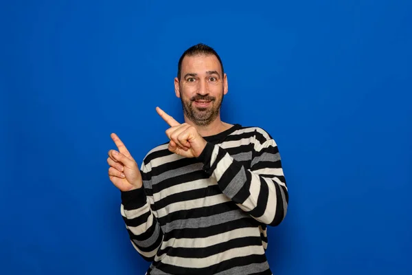 快乐的笑容40岁的男子穿着拉斯毛衣 用食指指向旁边 在模拟的工作区孤立的蓝色背景工作室的肖像 人的生活方式概念 — 图库照片