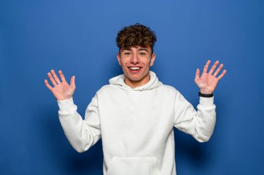 Heyecanlı sıradan bir adamın portresi. Elleri havada ve mavi arka planda izole edilmiş kameraya bakıyor.