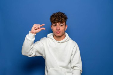 Mutsuz genç bir adam hayal kırıklığına uğramış görünüyor ve küçük bir jest yapıyor, küçük bir miktar ya da küçülme işareti, birkaç santim. Mavi arka planda kapalı stüdyo çekimi
