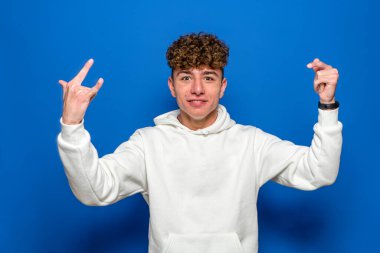 Mavi arka planda izole edilmiş kıvırcık saçlı yakışıklı genç bir adam çılgın bir ifadeyle elleri havada bir kaya sembolü yaparken çığlık atıyor. Müzik yıldızı konsepti