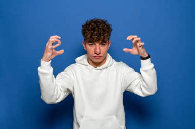 Mutlu bir gencin portresi. İki eliyle işaret ediyor. Mavi arka plandaki kameraya bakıyor.