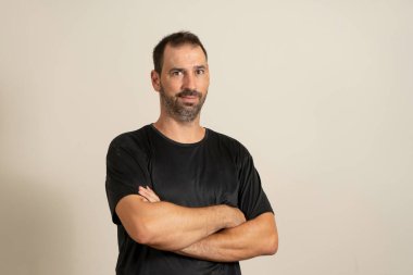 Bearded latin man posing funny with crossed arms isolated on beige studio background