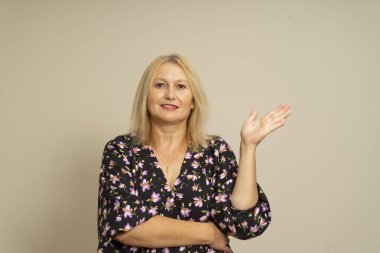 Sarışın ve koyu renk desenli elbisesi olan beyaz güzel bir kadın bir elinde cömertlik ve konukseverliğin göstergesi olarak bej arka planda izole edilmiş bir şey sunuyor..