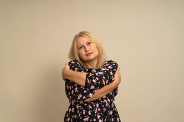 Bej arka planda koyu renk desenli elbiseli güzel sarışın kadın. Mutlu ve pozitif kucaklaşmalar, kendinden emin gülümsemeler. Kendini sevmek ve araba kullanmak.