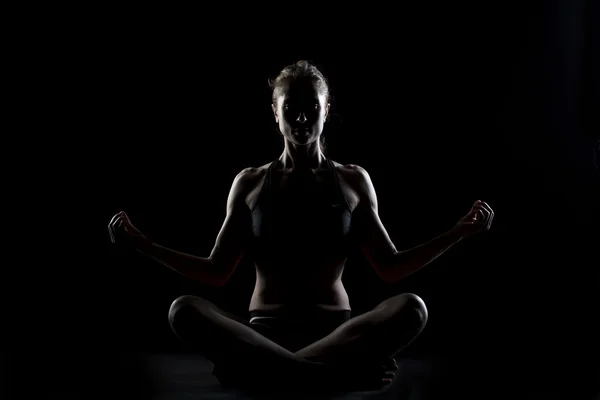 Una mujer caucásica haciendo ejercicio de yoga meditando en estudio de silueta sobre fondo negro Imagen De Stock