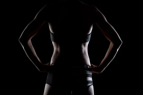 Visão traseira da mulher em forma posando com costas atléticas em fundo preto. sexy jovem feminino fisiculturista mostrando ela muscular de volta . Imagem De Stock
