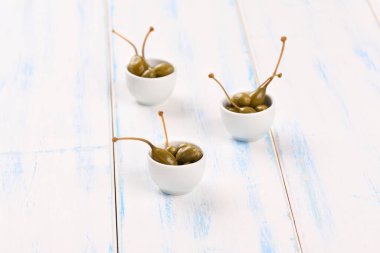 Beyaz arka planda küçük beyaz bir kasede kapari..