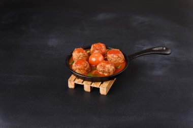 Koyu arkaplanda tencerede domates soslu köfte..