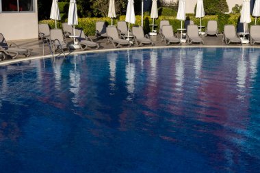 Boş güneşlenirler havuzun yanında mavi suyla