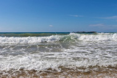 Köpüklü turkuaz dalgalar kumsalda yuvarlanıyor.