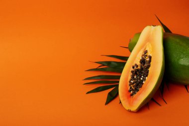 Turuncu arka planda yaprakları olan olgun papaya.
