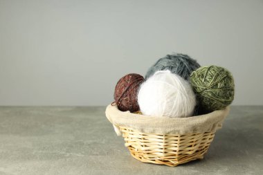 Açık gri masada yün yumakları olan hasır sepet.