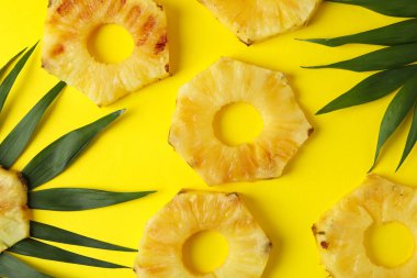 Sarı arka planda ızgara ananas dilimleri ve yapraklar..
