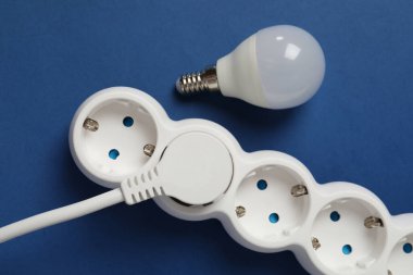 Mavi arkaplanda enerji tasarrufu ampulü ve güç şeridi.