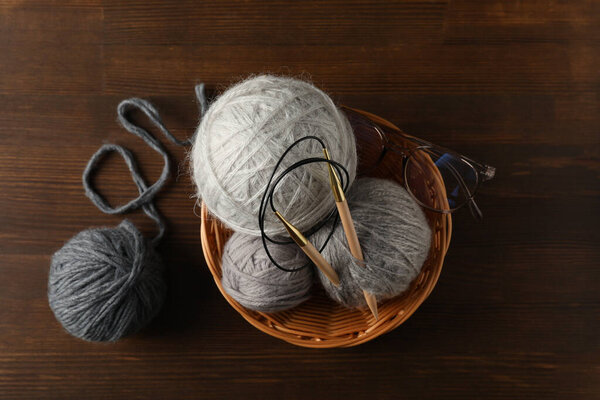 Плетеная миска с пряжей шары и вязальные спицы, и очки на деревянном фоне