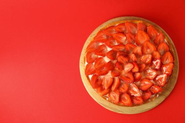 Kırmızı arka planda çilekli turta ile yuvarlak tahta.