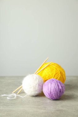 Açık gri arka planda örgü iğneleri olan çok renkli iplik topları..