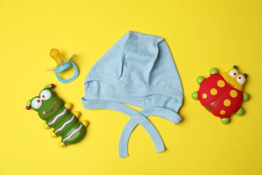 Sarı arka planda bebek şapkası ve oyuncaklar.