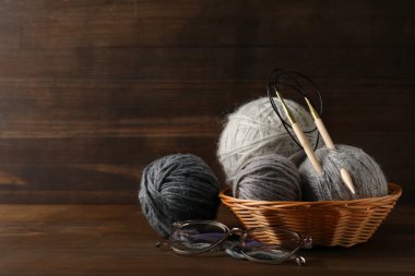Hasır sepette örgü iğneleriyle ahşap bir arka planda çok renkli iplik yumakları..