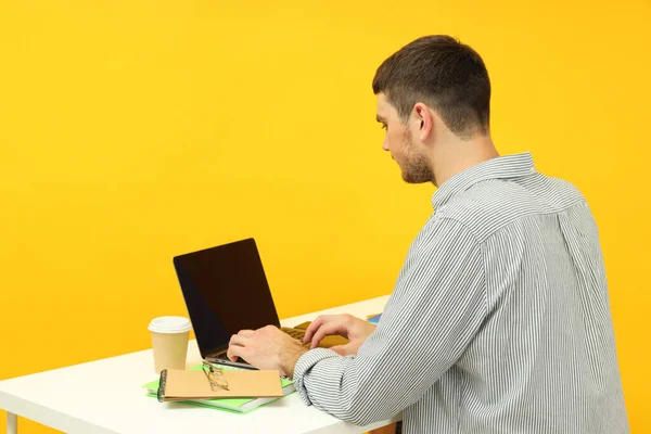 黄色の背景にテーブルの上に座っている若い男と勉強の概念 — ストック写真