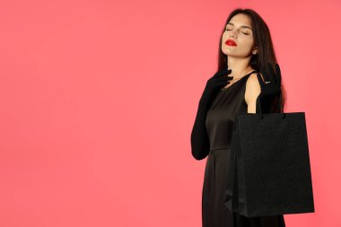 Pembe arka planda kese kağıtları olan siyah elbiseli çekici bir kız..