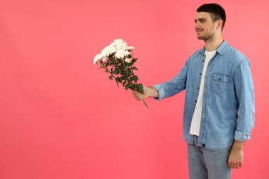 Genç adam pembe arka planda çiçek veriyor..