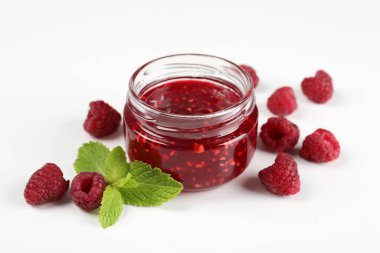 Bir kavanoz ahududu reçeli ve beyaz arka planda malzemeleri var.