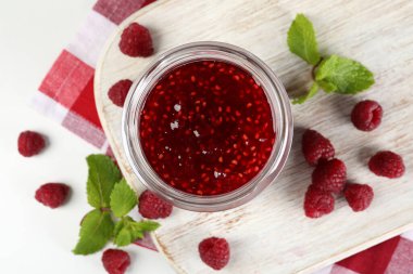 Ahududu reçeli kavanozu ve beyaz ahşap tezgahta malzemeler.