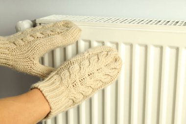 Eldivenli kadın elleri radyatörün yanında durur..